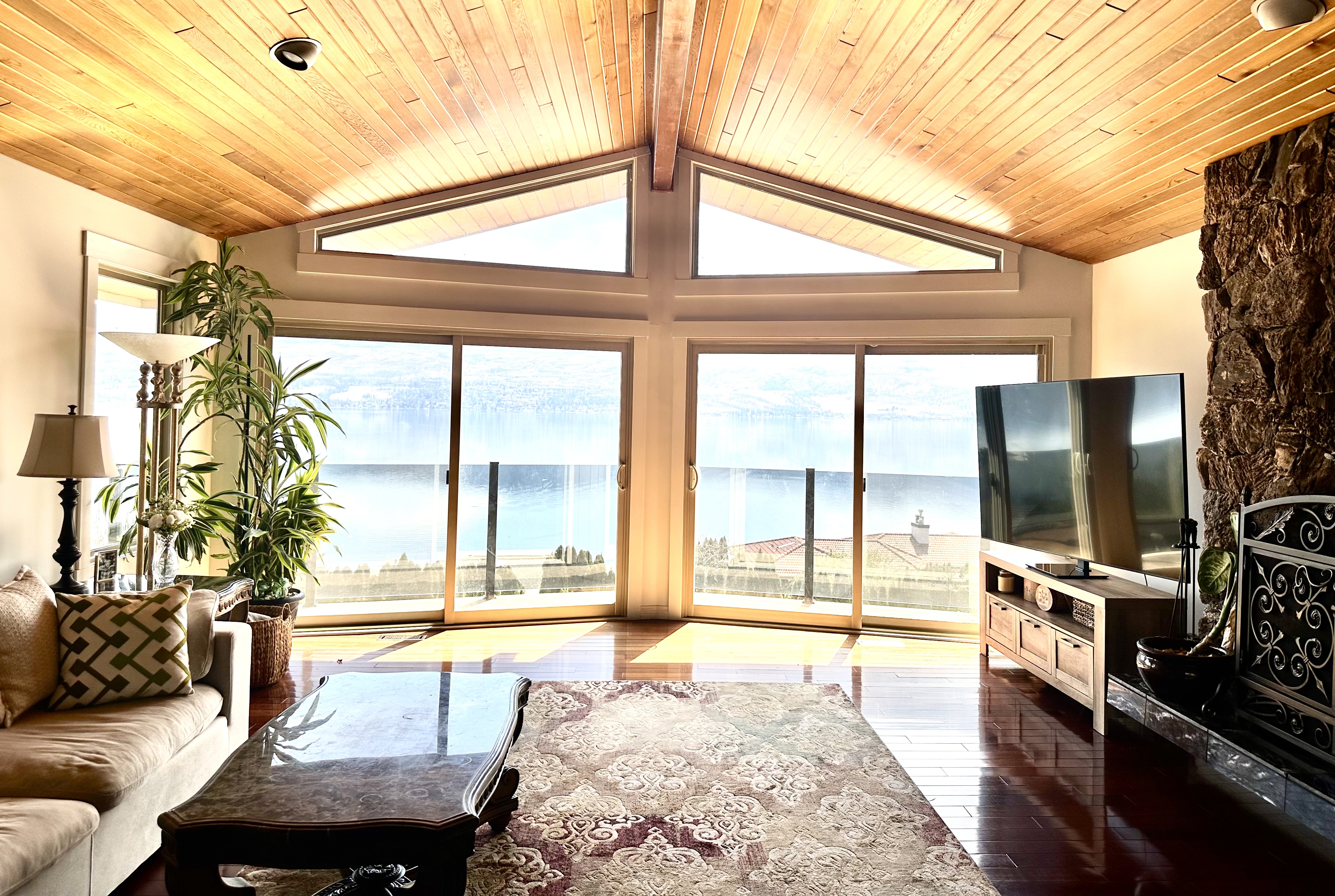 Vaulted living room with panoramic lake view windows, stone fireplace and leather sofa