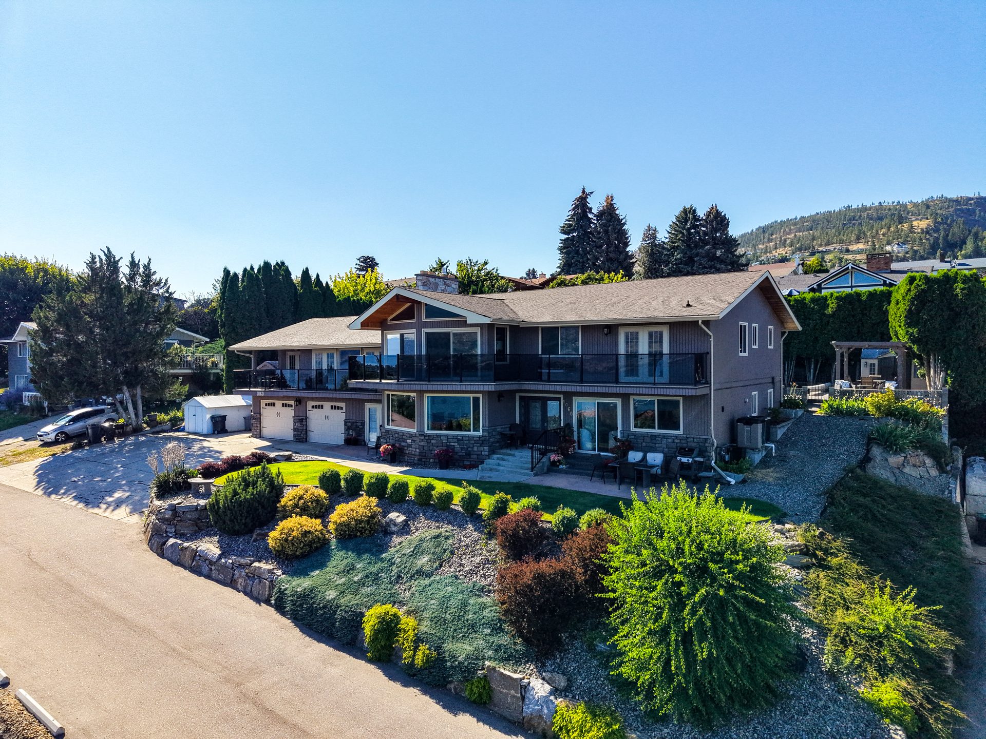 Drone aerial of property exterior showing landscaped front yard and glass-railing balcony