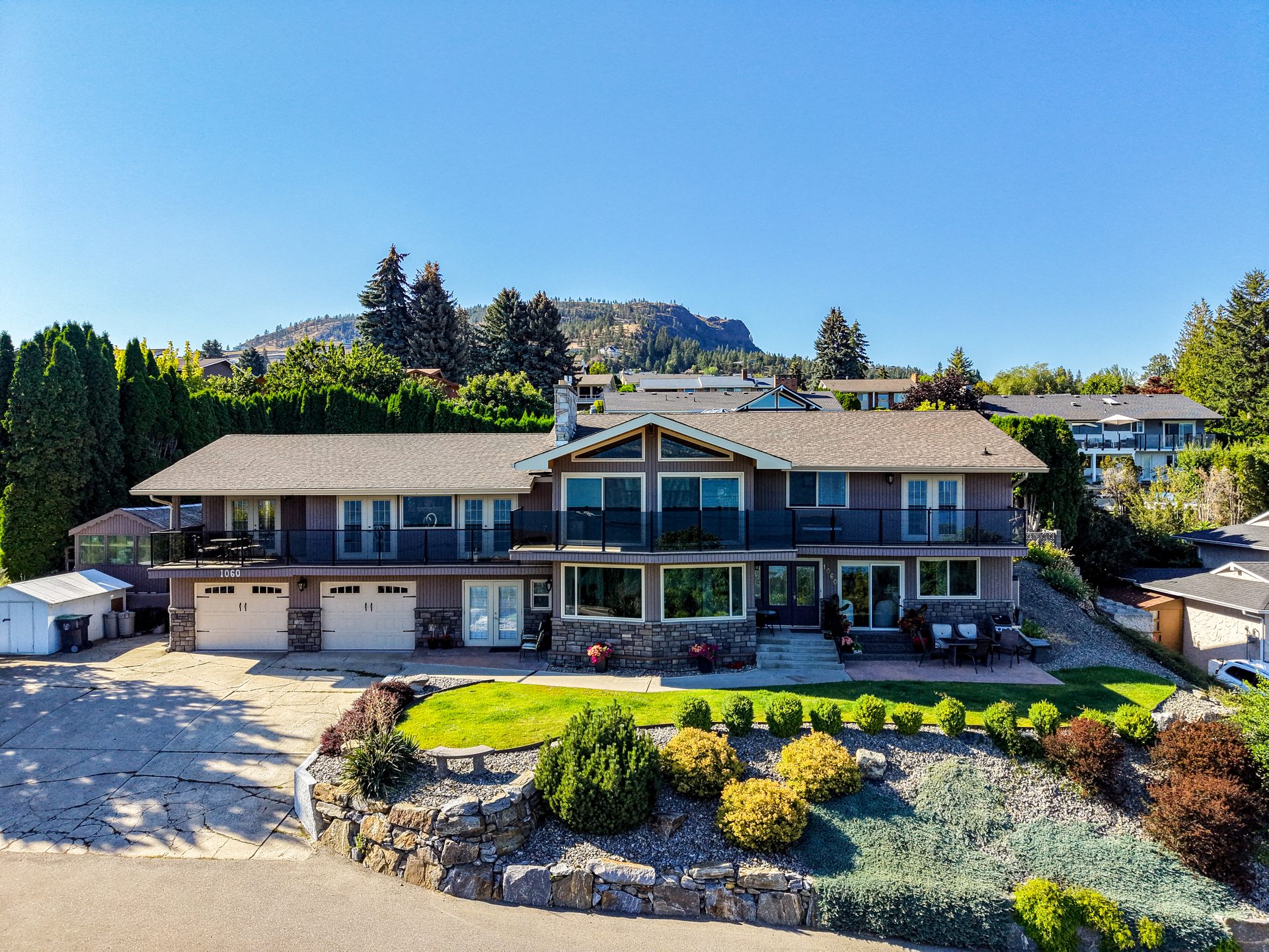 Aerial front view of home with stone facade, glass-railing balcony and mountain backdrop
