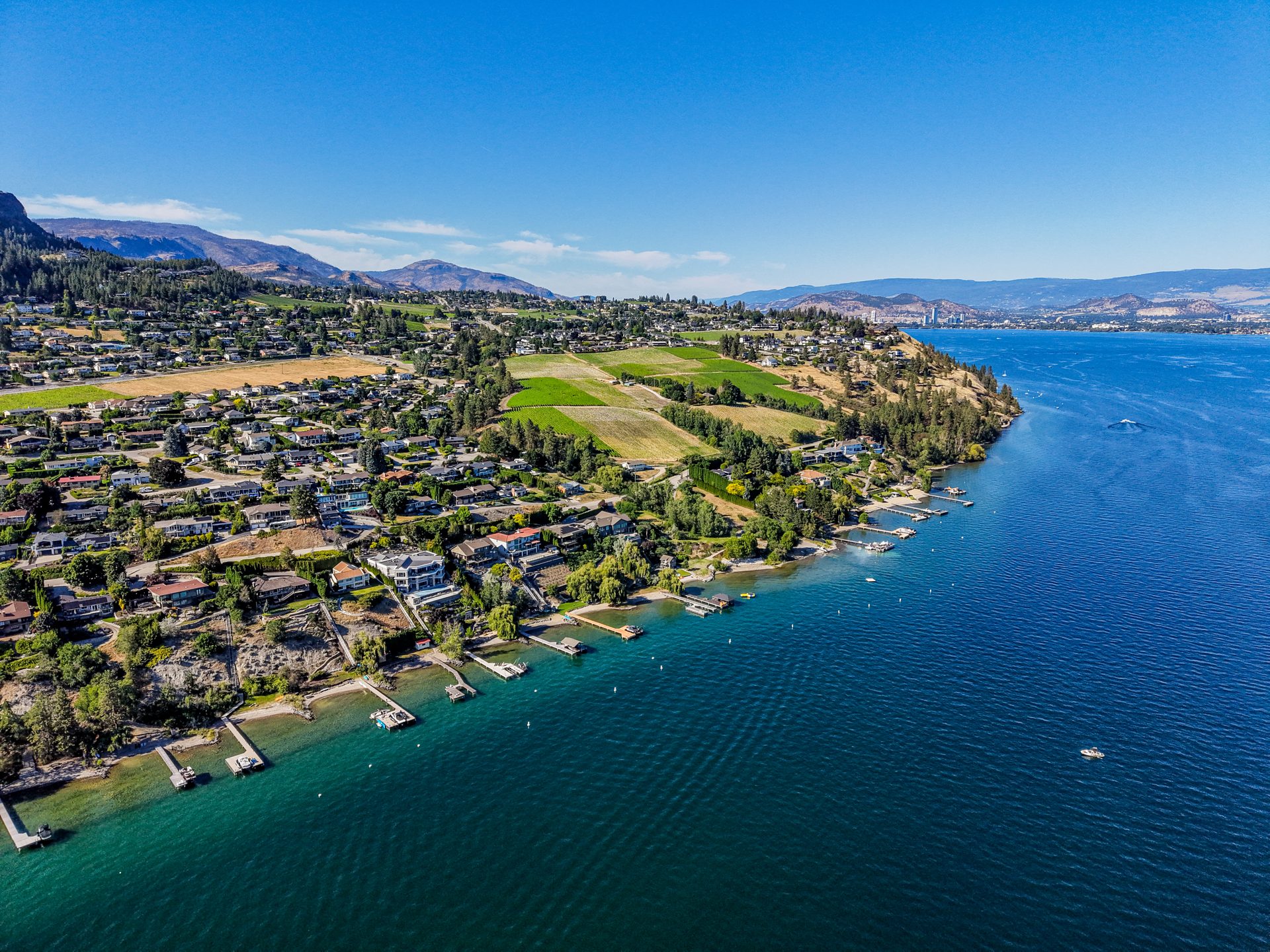 Aerial of Okanagan Lake with boats and sparkling water, mountains on horizon