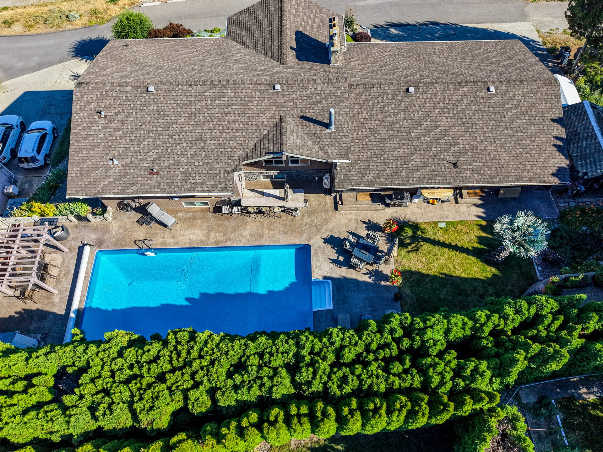 Drone view of private pool, patio dining and lush hedged backyard