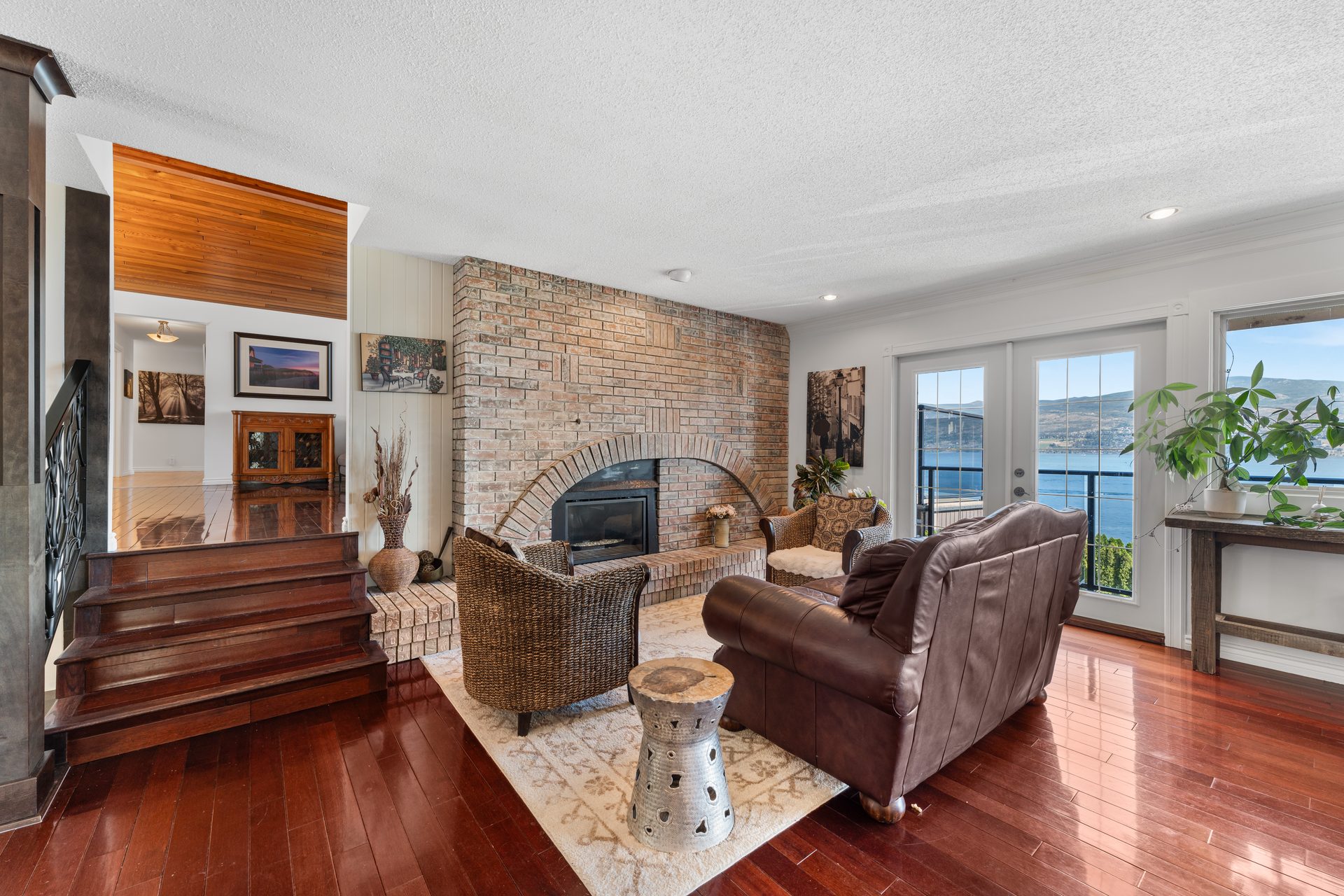 Living room with brick fireplace, leather sofa, wicker chairs and Okanagan Lake view