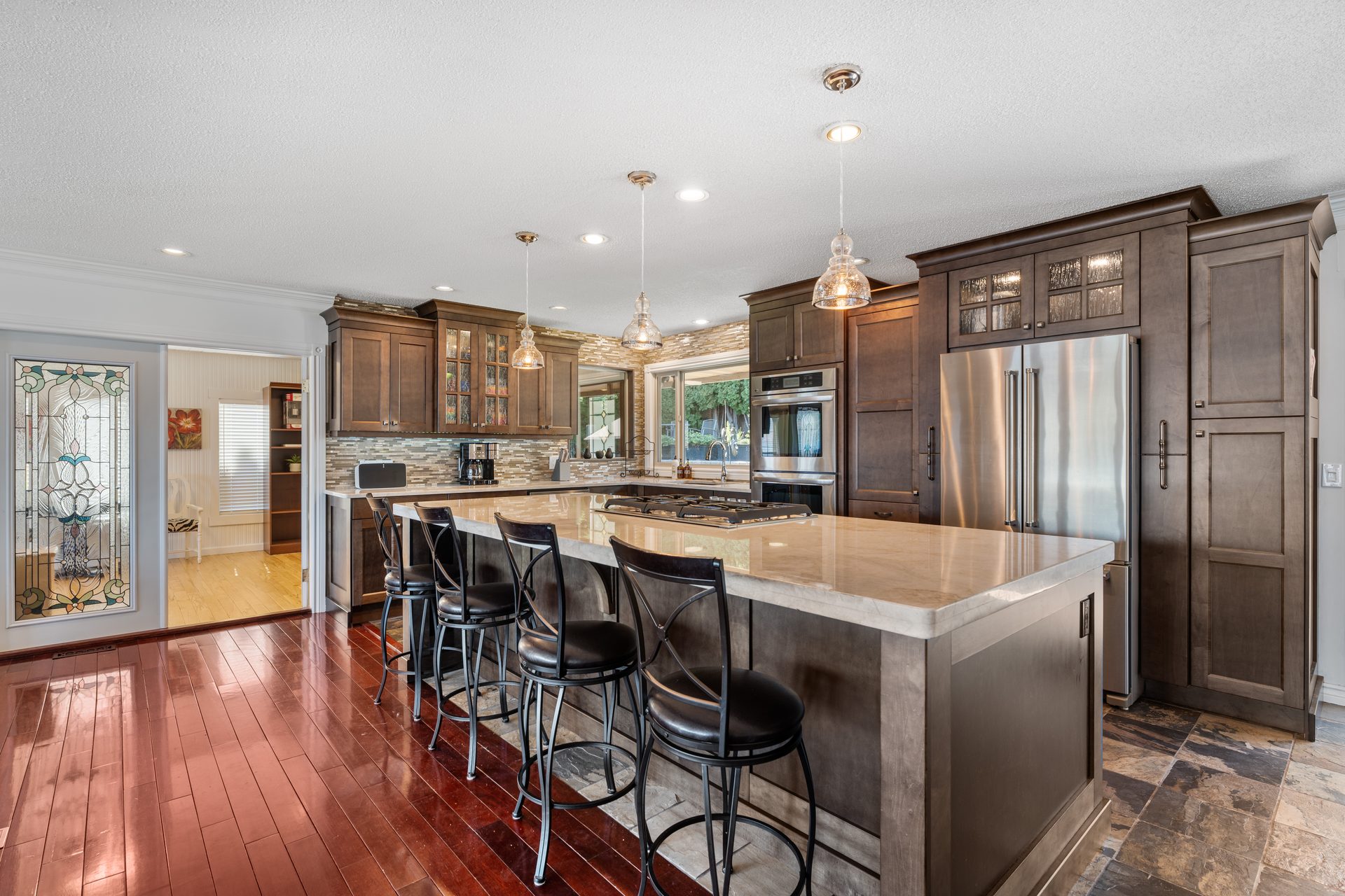 Kitchen island with marble countertop, pendant lights, stained glass feature and stainless refrigerator
