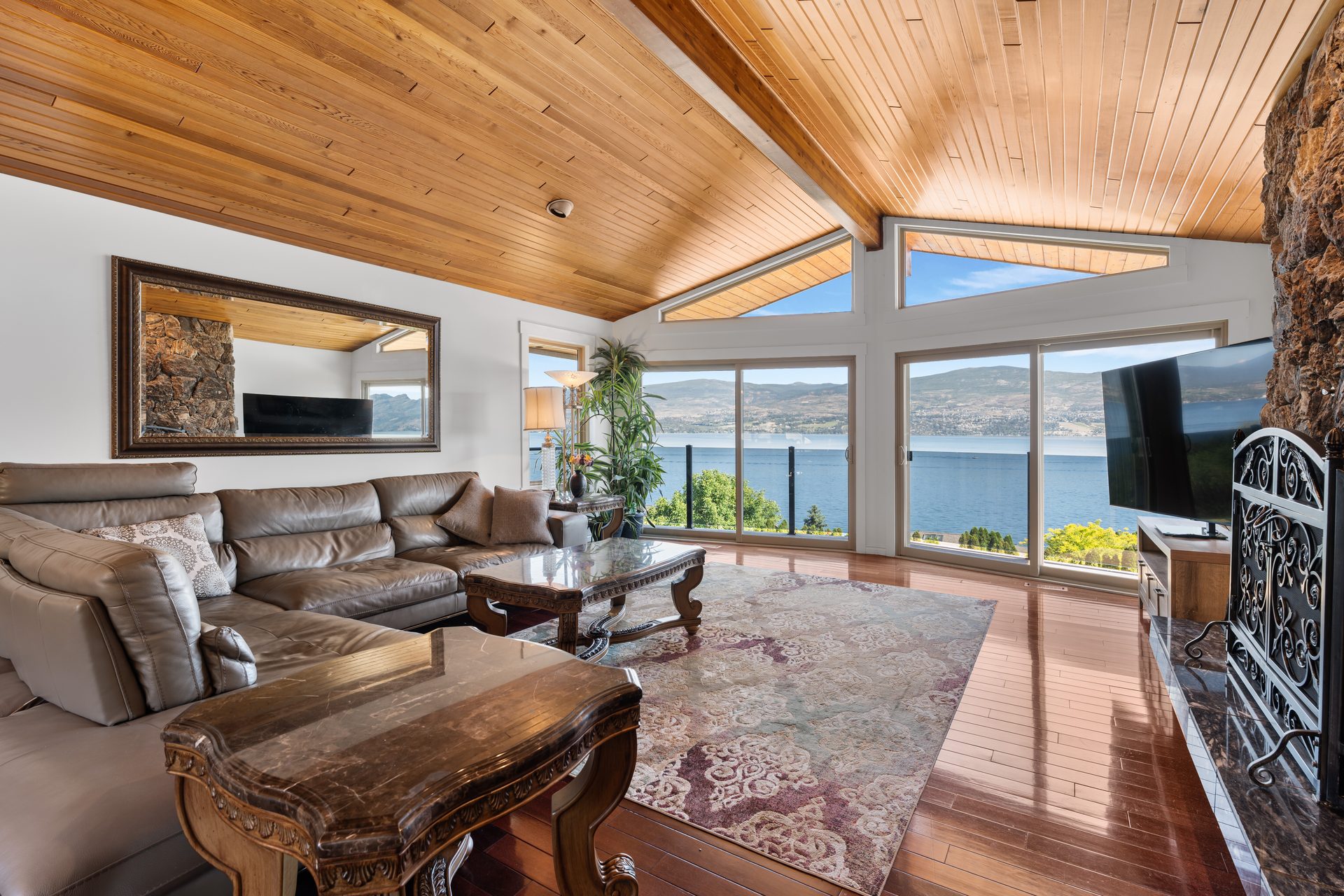 Vaulted great room with panoramic Okanagan Lake view, stone fireplace and leather sectional