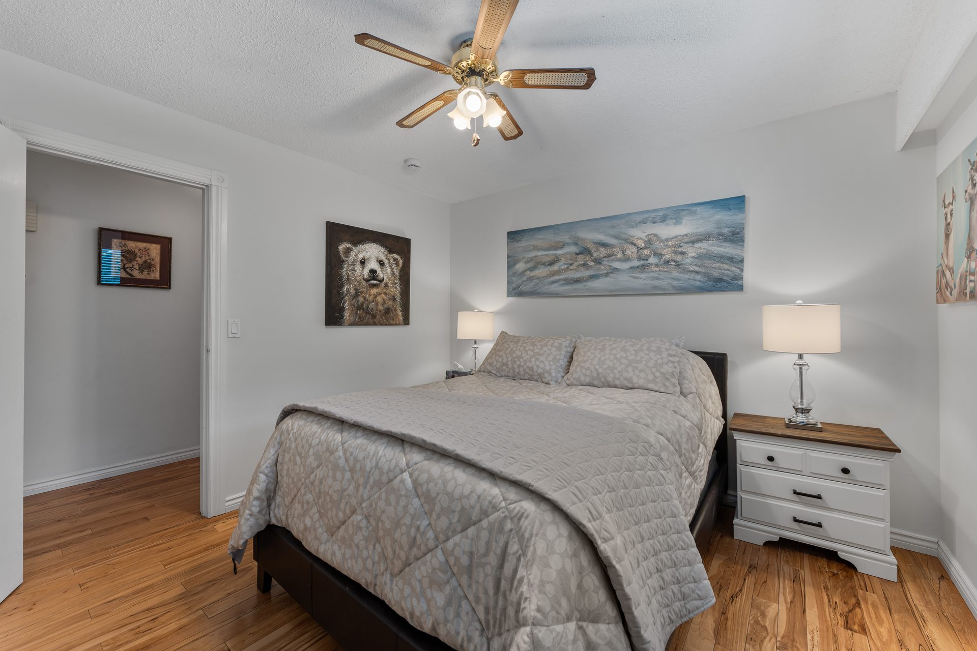 Queen bedroom with wildlife artwork, wood floors and ceiling fan
