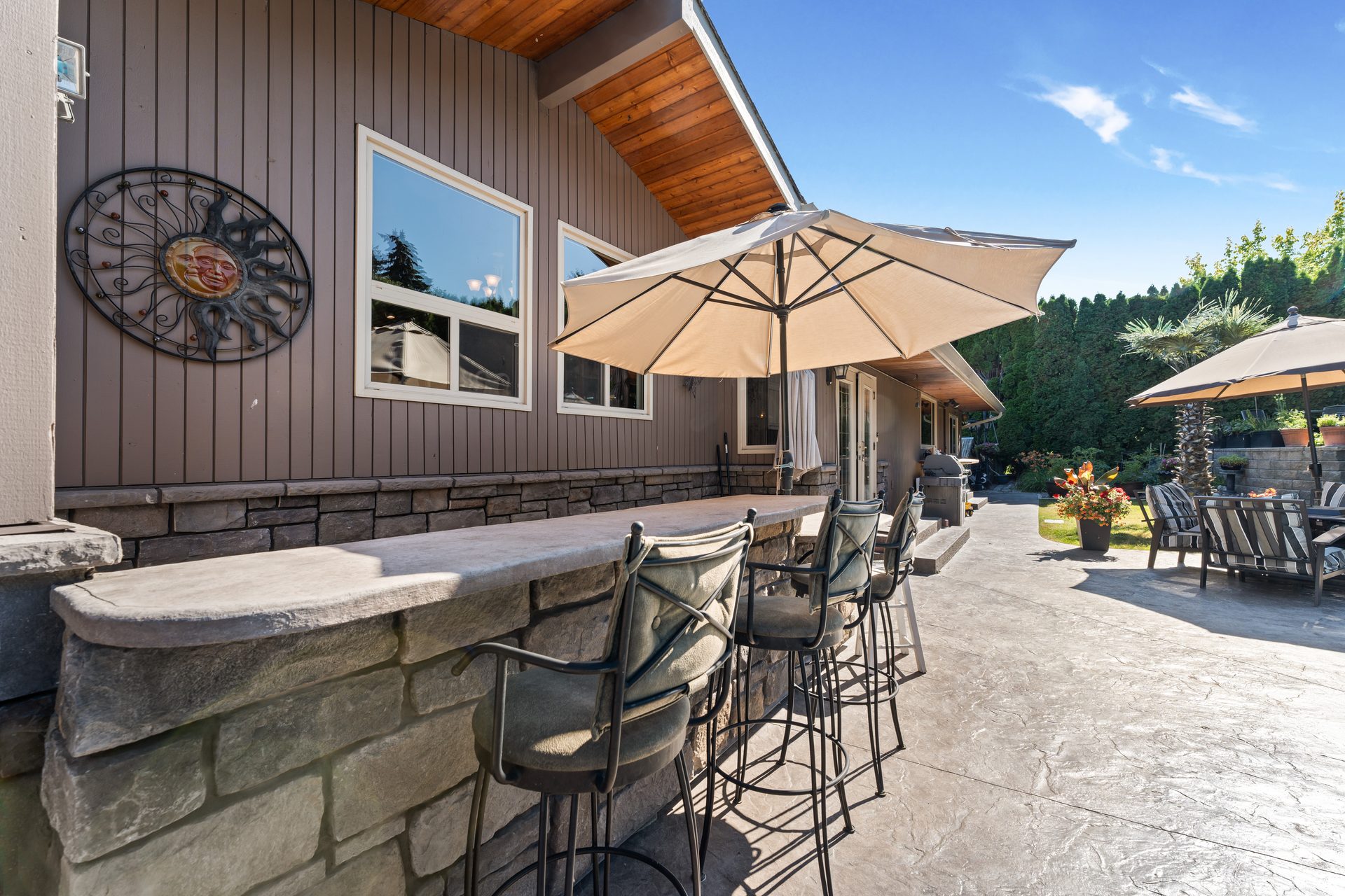 Outdoor stone bar with bar stools, patio umbrella and garden beyond