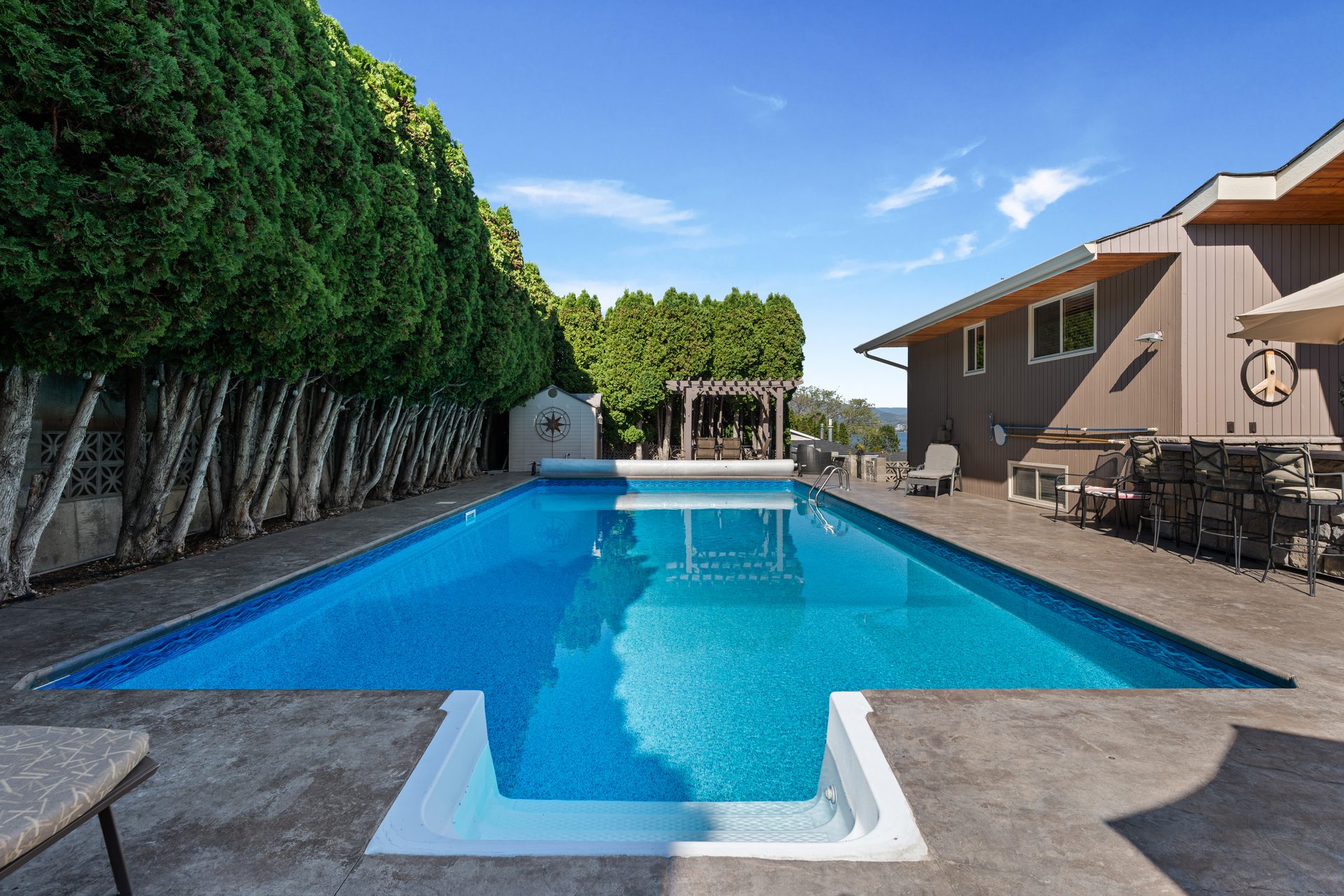 Lower patio lounge with blue sofa, raised herb garden planters and pool view beyond